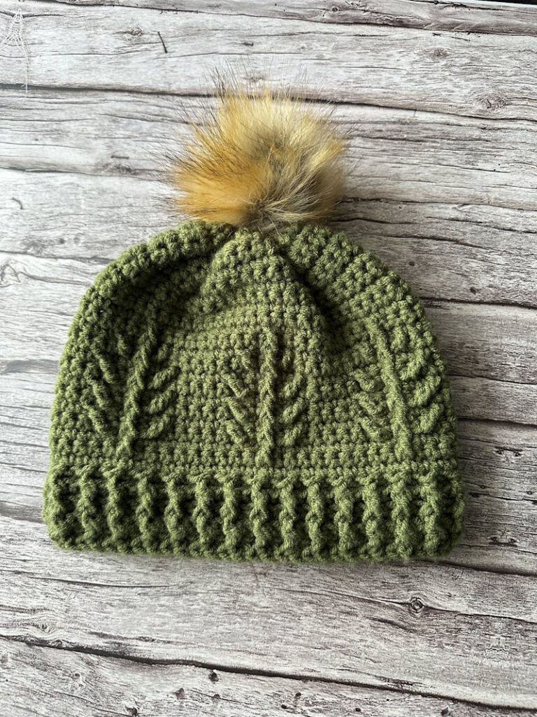 Textured evergreen crochet winter hat with pom pom and front post stitch pattern