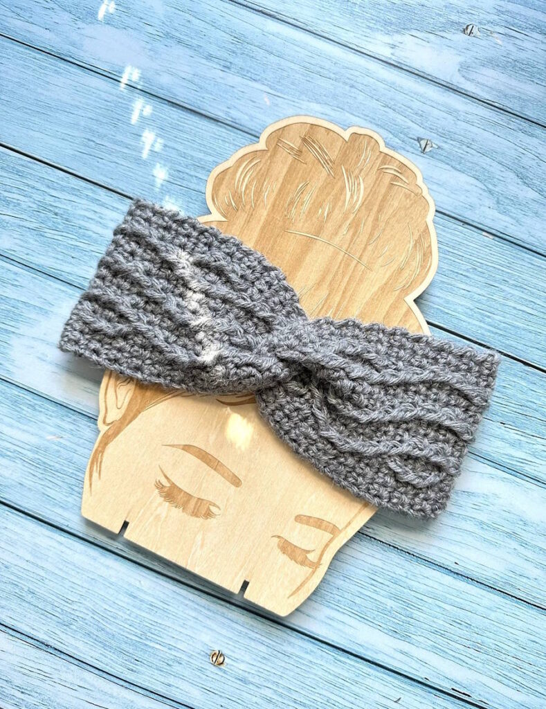 Cable weave crochet headband shown on a wooden display, a textured winter ear warmer for women