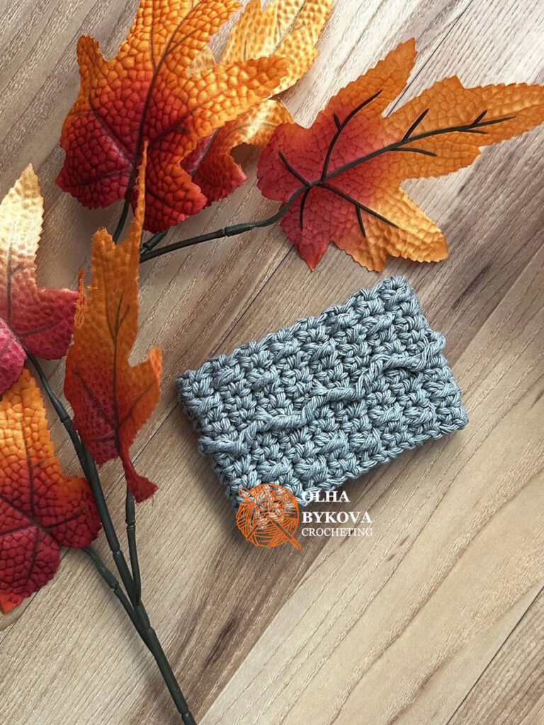 Textured crochet cup cozy Mountain Trail pattern, coffee sleeve design with soft cable style stitches on wooden background