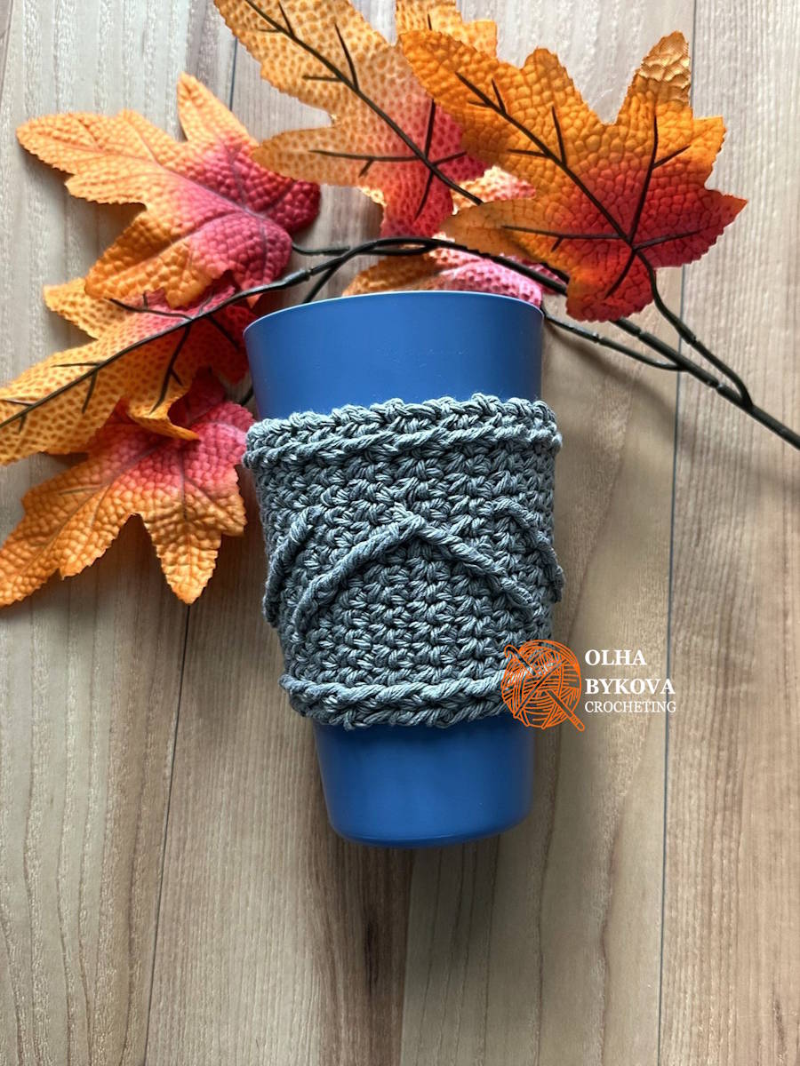Crochet cup cozy with chevron ridge texture on coffee cup, textured cable style crochet coffee sleeve with autumn leaves background
