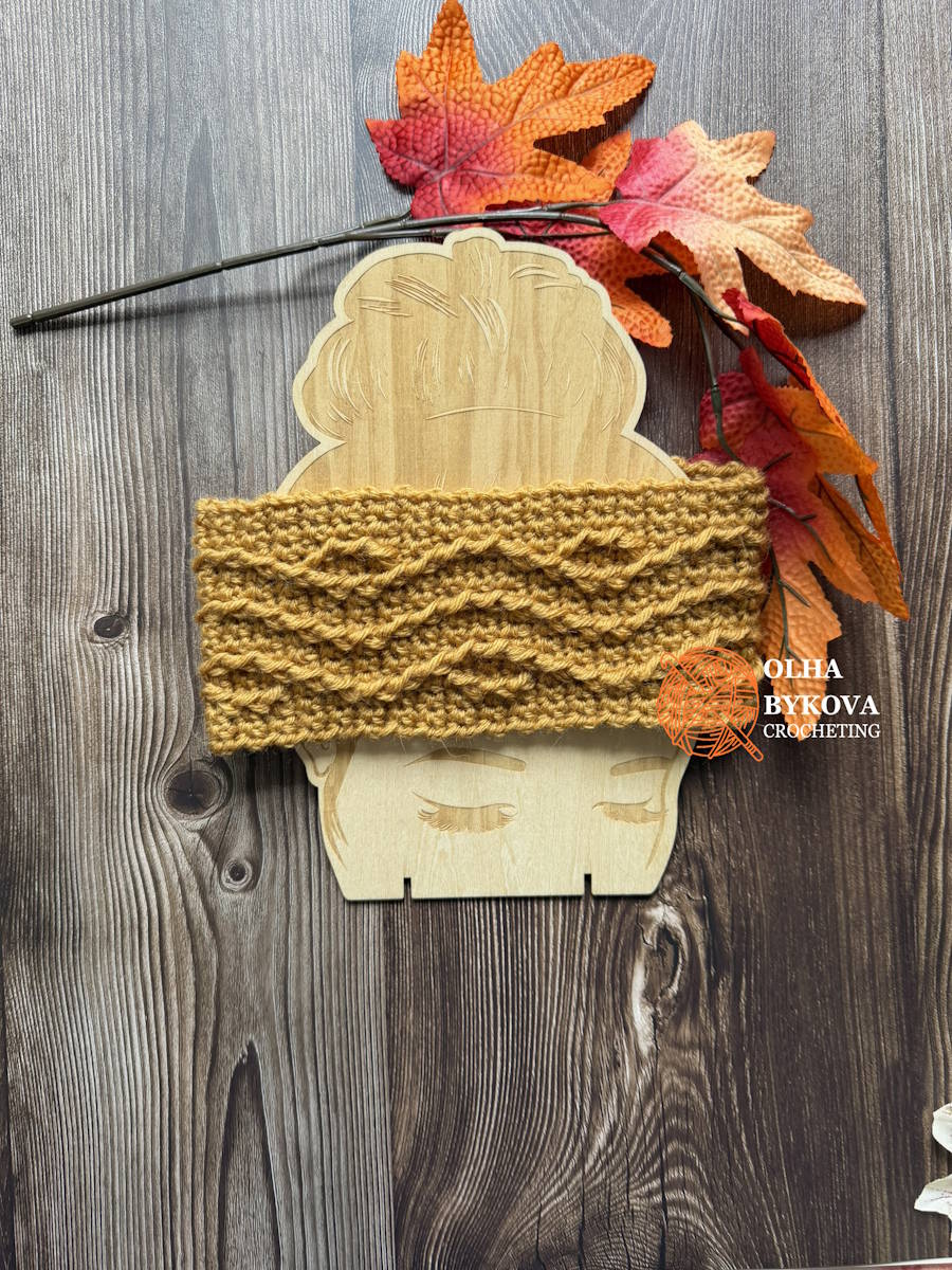 Cable crochet headband pattern shown flat on a wooden mannequin with autumn leaves